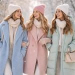 Három nő pasztell színű kabátokban sétál a hóban